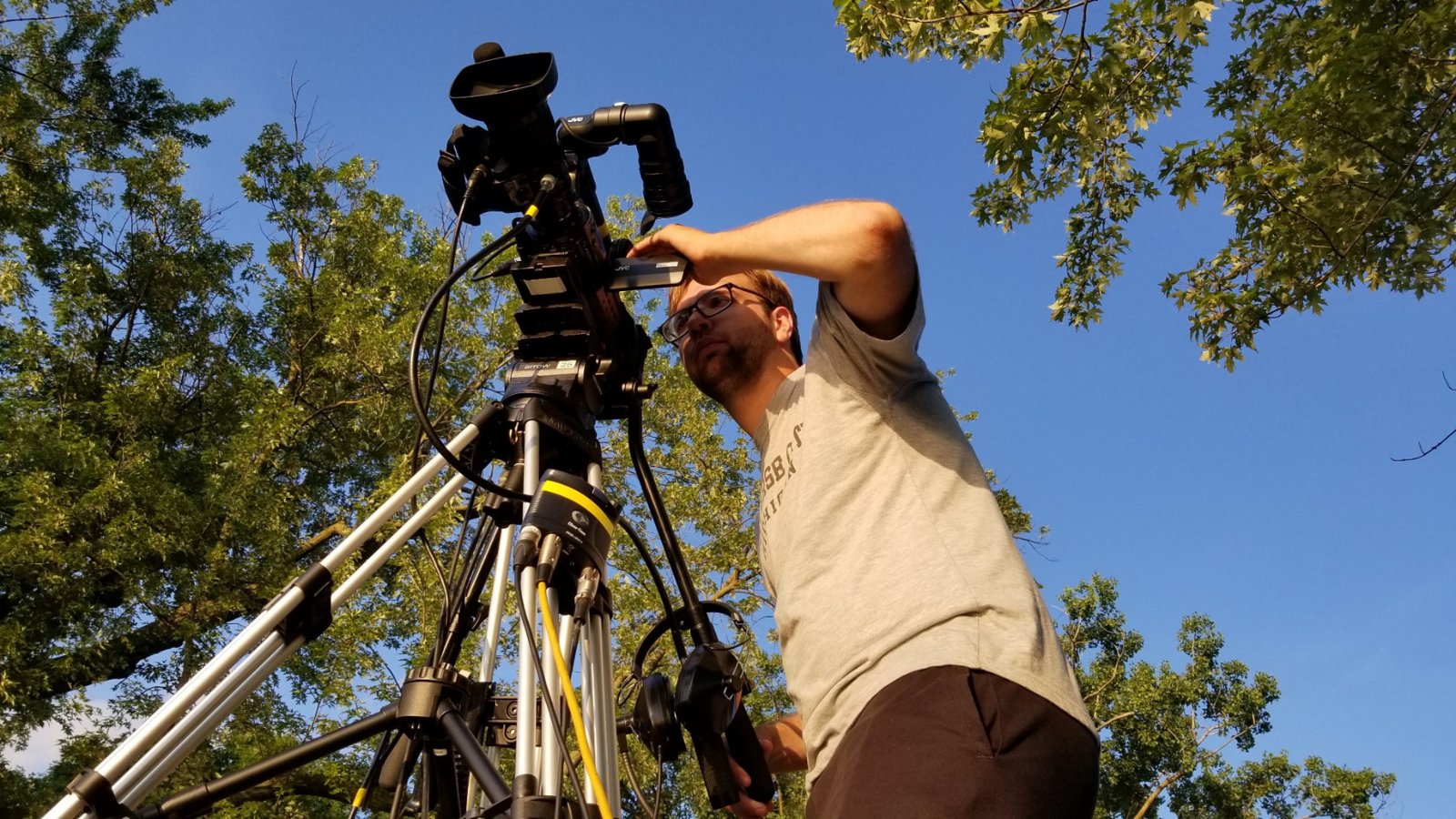 Ashton Gillett operating a shoulder camera on a tripod outdoors